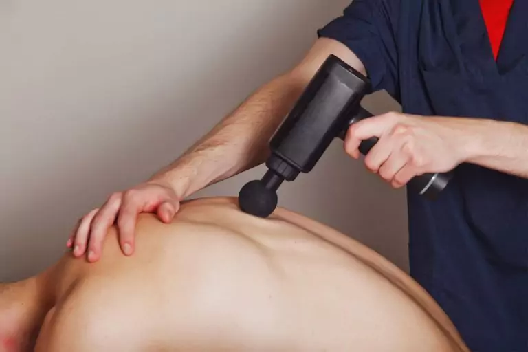 physiotherapist using massage gun on patients back